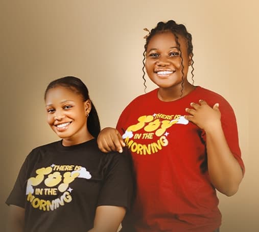 Two smiling women wearing ADULLAM “There Is Joy in the Morning” T-shirts in black and red.